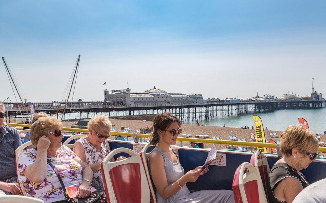 Brighton Hop-On Hop-Off bus passengers with Brighton Pier in the background.