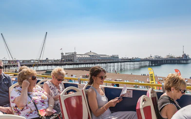 Brighton Hop-On Hop-Off bus passengers with Brighton Pier in the background.