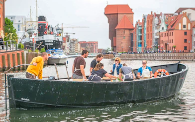 Guests tasting pierogi on a boat during Motława River cruise in Gdansk, with historic buildings in view.