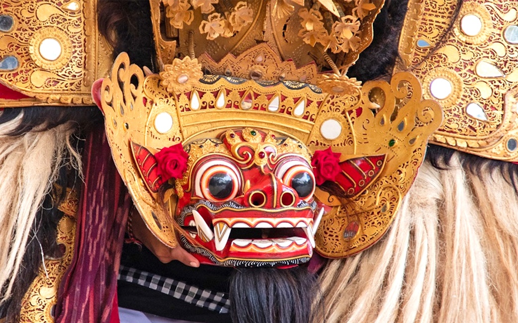 Balinese Barong mask with intricate gold details and red accents.
