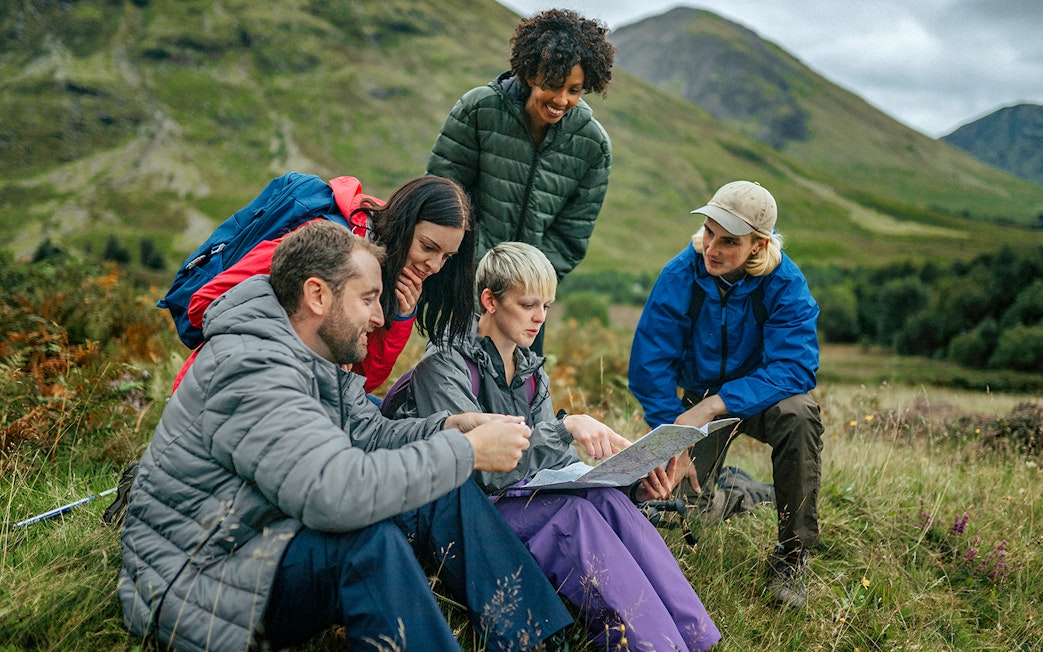 Tour guide explaining map to tourists in a scenic mountain landscape.