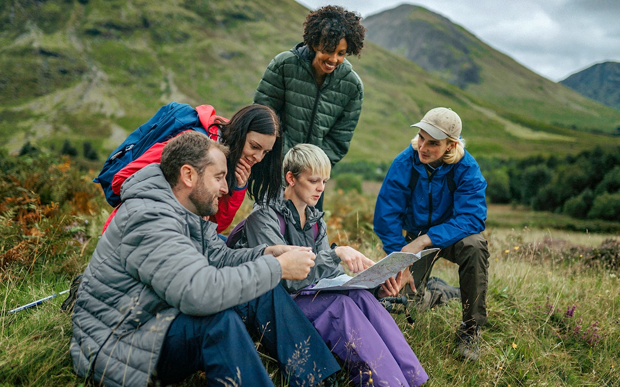 Tour guide explaining map to tourists in a scenic mountain landscape.