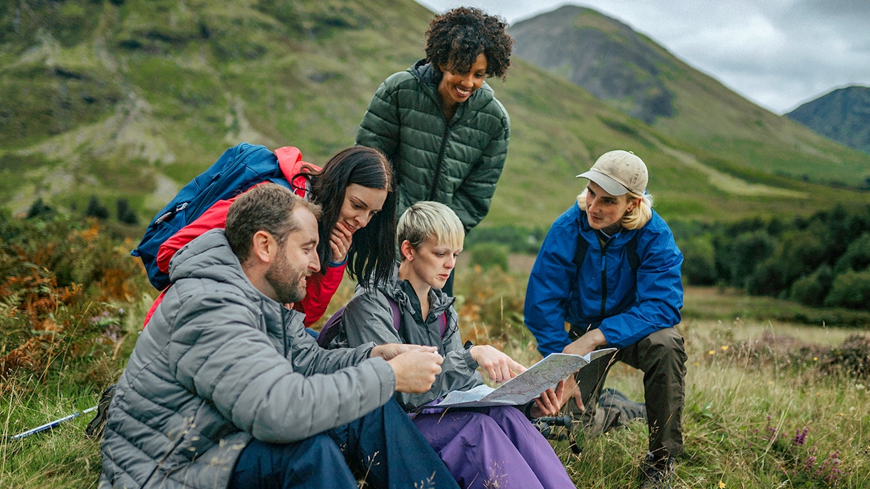 Tour guide explaining map to tourists in a scenic mountain landscape.