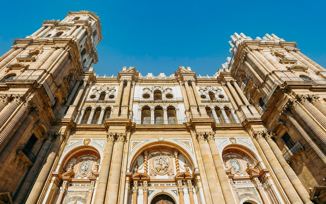 Málaga Cathedral facade with detailed architecture under a clear blue sky.