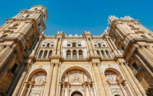 Málaga Cathedral facade with detailed architecture under a clear blue sky.