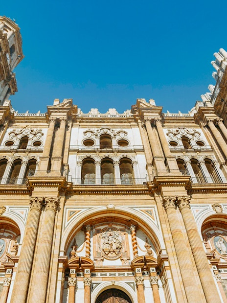 Málaga Cathedral facade with detailed architecture under a clear blue sky.
