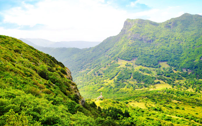 Lush green landscape of Piton de la Petite Rivière Noire, Mauritius, with rolling hills and distant peaks.