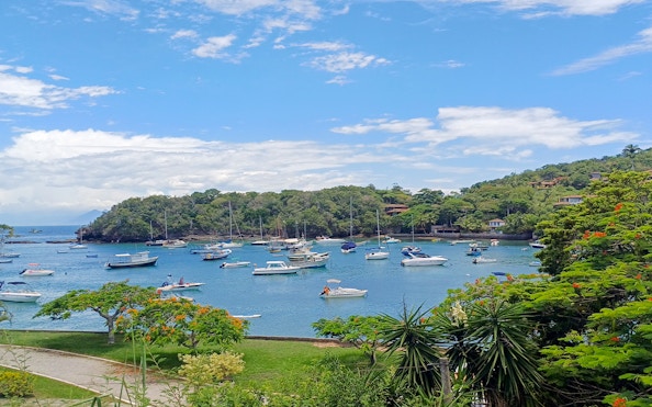 Boats anchored at Praia da Azedinha, Armação dos Búzios, with lush greenery and clear blue sky.