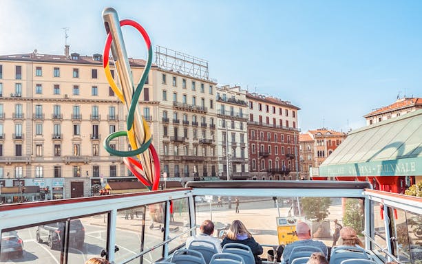 Open-top bus tour passing by the Needle, Thread and Knot sculpture in Milan.