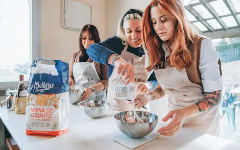 Participants making fresh pasta in a cooking class, measuring ingredients into bowls.