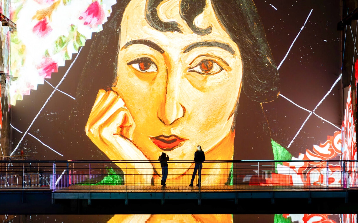 Matisse artwork projection at Bassins Des Lumieres exhibition with visitors on a bridge.