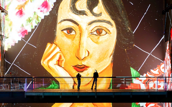 Matisse artwork projection at Bassins Des Lumieres exhibition with visitors on a bridge.