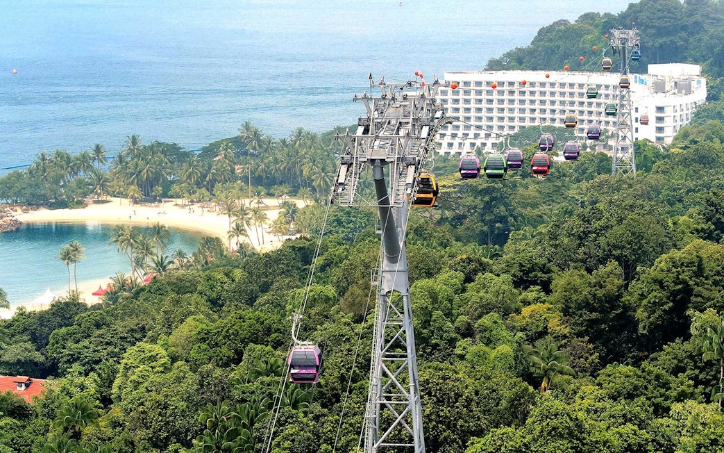Cable cars over lush greenery and beach in Sentosa, Singapore.