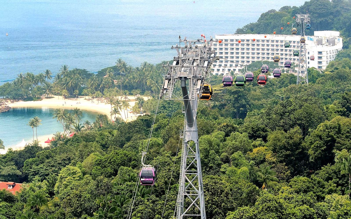 Cable cars over lush greenery and beach in Sentosa, Singapore.