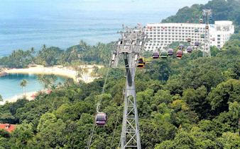 Cable cars over lush greenery and beach in Sentosa, Singapore.