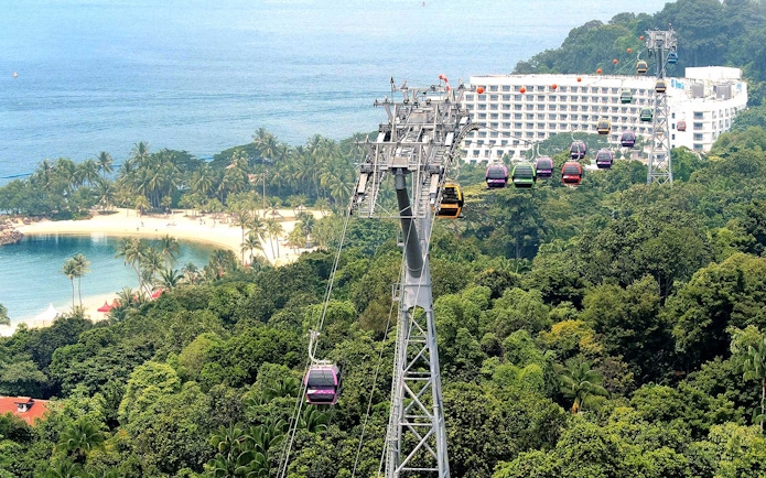Cable cars over lush greenery and beach in Sentosa, Singapore.