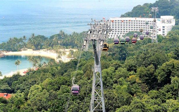 Cable cars over lush greenery and beach in Sentosa, Singapore.