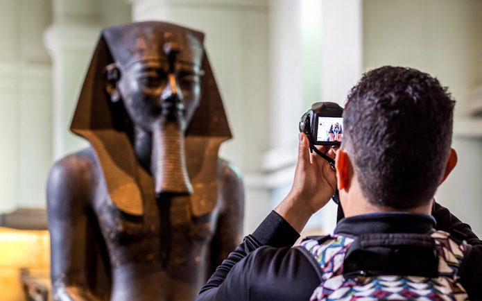 Visitor photographing an Egyptian statue at the British Museum.