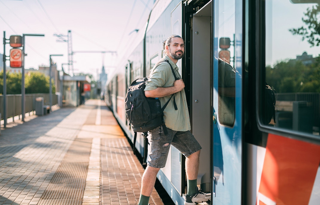 Man boarding a train at a sunny platform with a backpack.