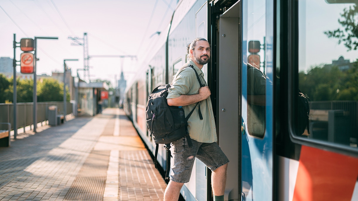 Man boarding a train at a sunny platform with a backpack.