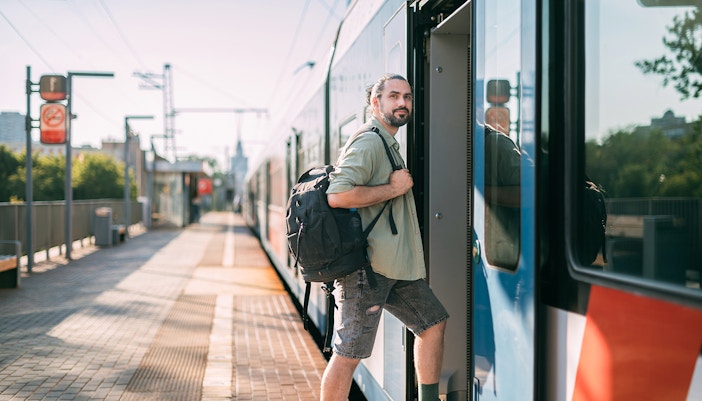 Man boarding a train at a sunny platform with a backpack.