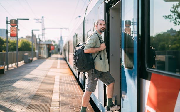 Man boarding a train at a sunny platform with a backpack.