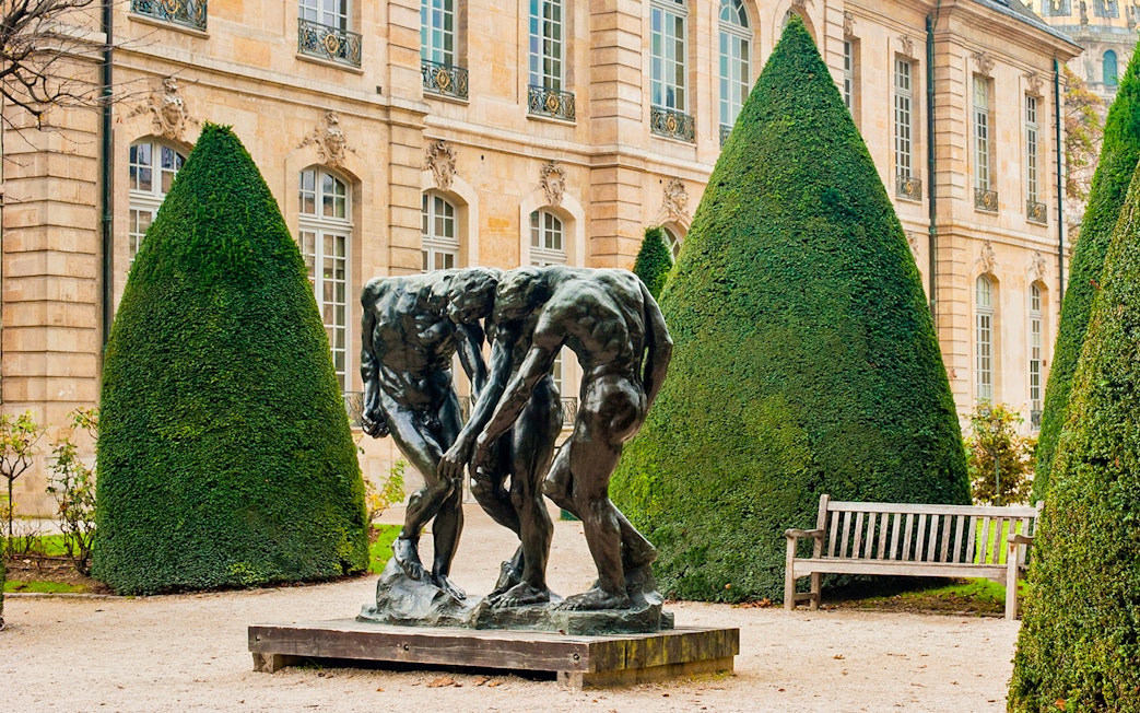 Rodin Museum garden with bronze sculpture surrounded by manicured trees.