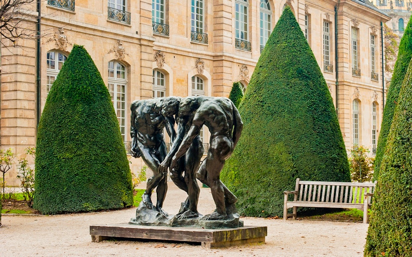 Rodin Museum garden with bronze sculpture surrounded by manicured trees.