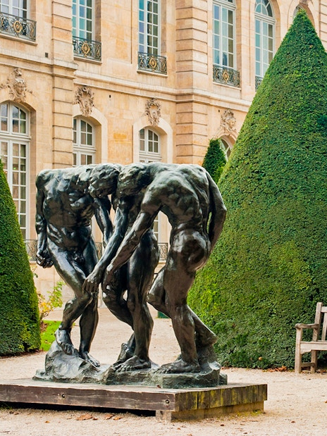 Rodin Museum garden with bronze sculpture surrounded by manicured trees.