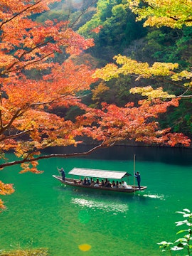 Boat tour on Kyoto's Hozu River surrounded by autumn foliage.