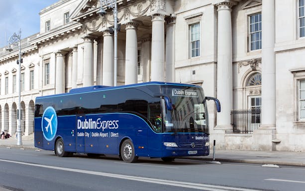 Dublin Express bus parked near a historic building, offering one-way tickets from Belfast to Dublin Airport.