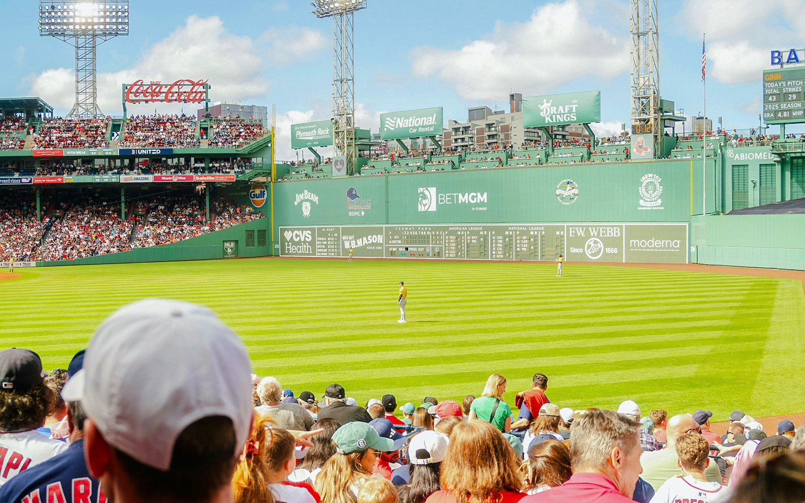 Crowd watching a baseball game at Fenway Park, Boston, with iconic Green Monster in view.