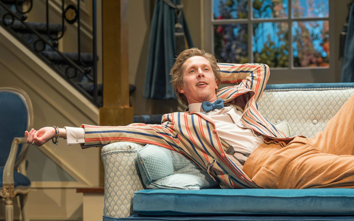 Actor lounging on a sofa during a performance of "Hay Fever" in West End theater.