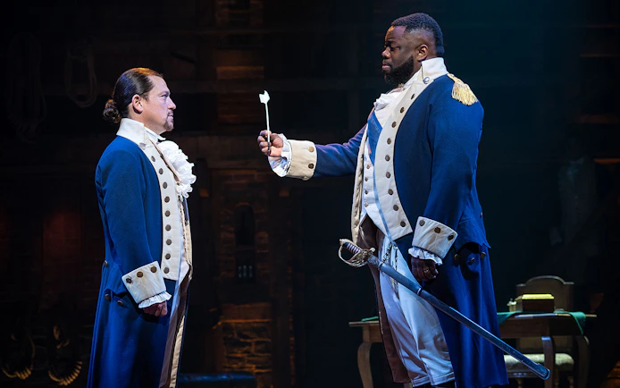Two actors in colonial costumes perform a scene from the musical Hamilton.