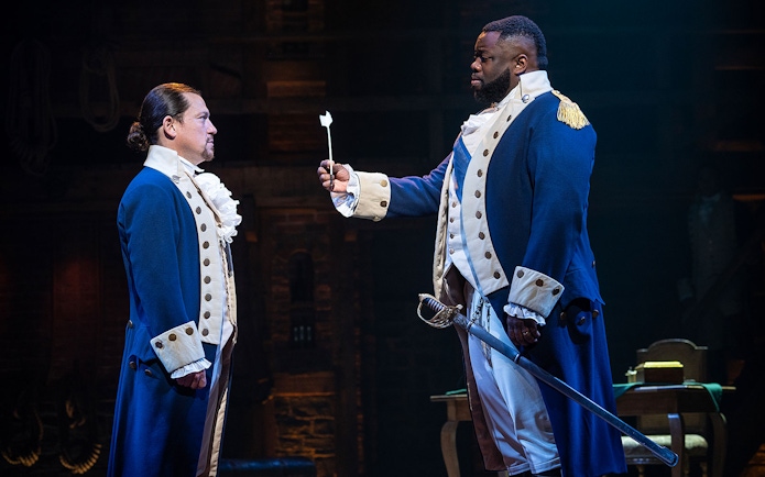 Two actors in colonial costumes perform a scene from the musical Hamilton.