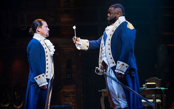 Two actors in colonial costumes perform a scene from the musical Hamilton.