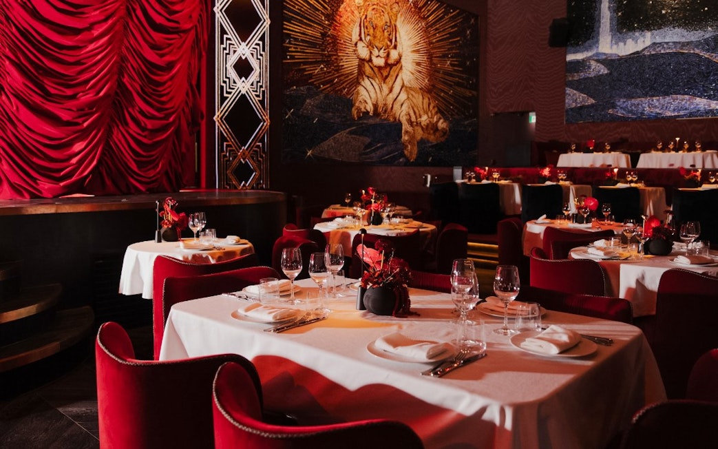 Dining tables with red chairs and elegant settings at Paris Paradis, featuring a tiger mural.