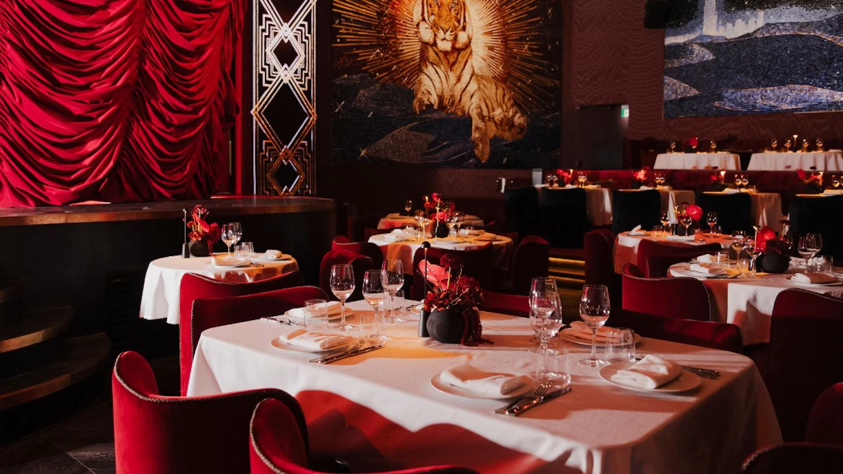 Dining tables with red chairs and elegant settings at Paris Paradis, featuring a tiger mural.