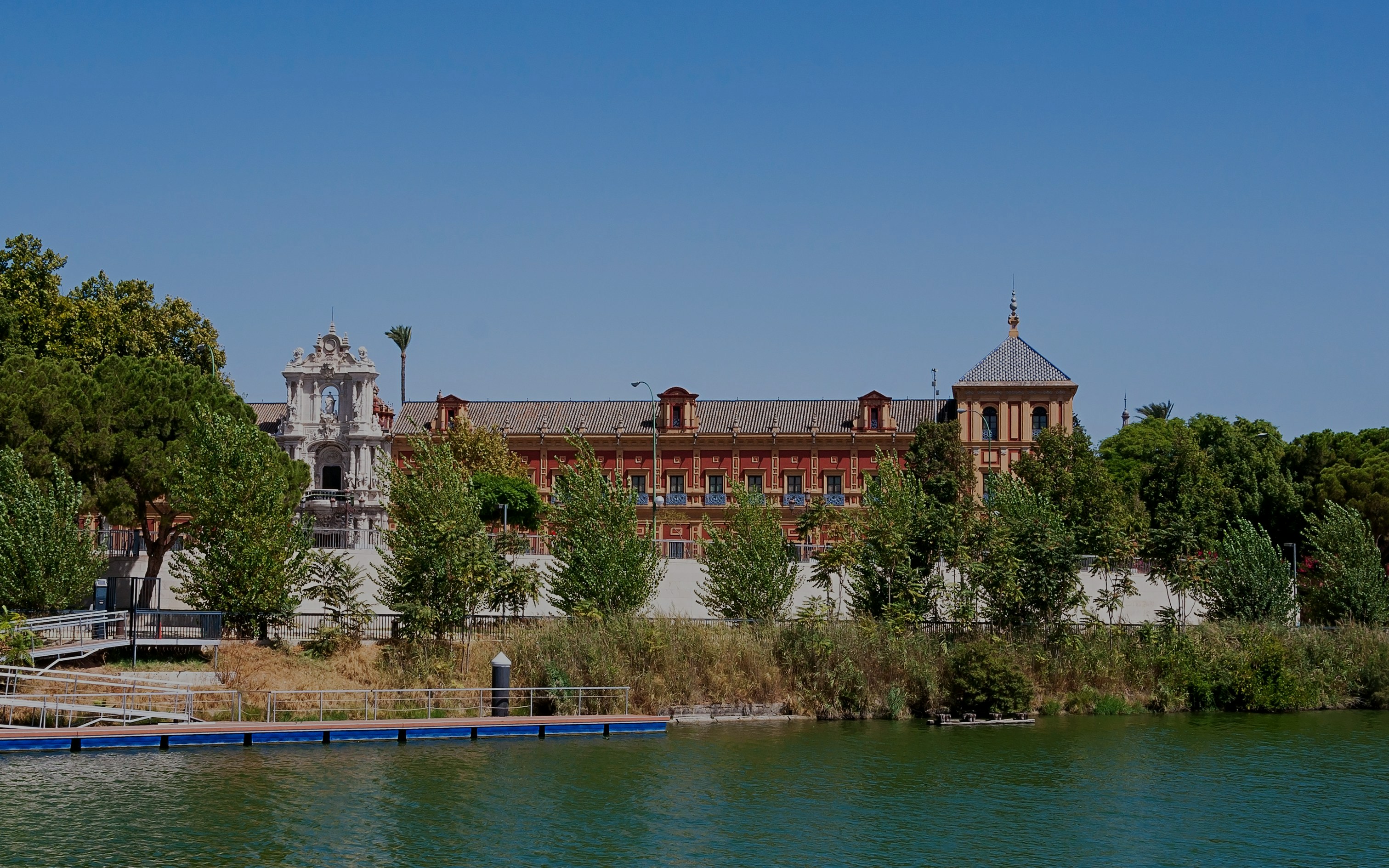 Palace of San Telmo viewed from the Guadalquivir River, Seville, surrounded by trees.