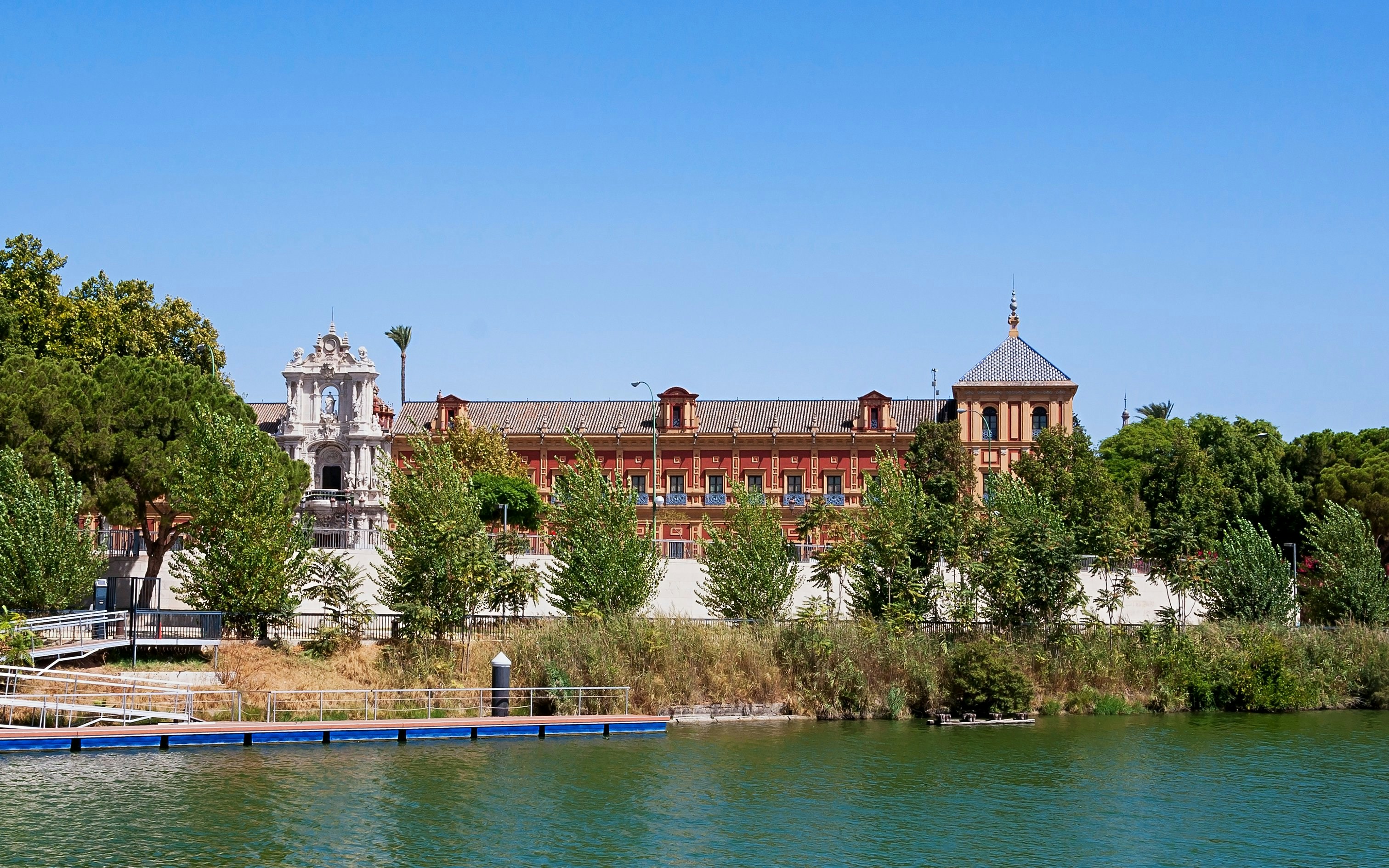 Palace of San Telmo viewed from the Guadalquivir River, Seville, surrounded by trees.