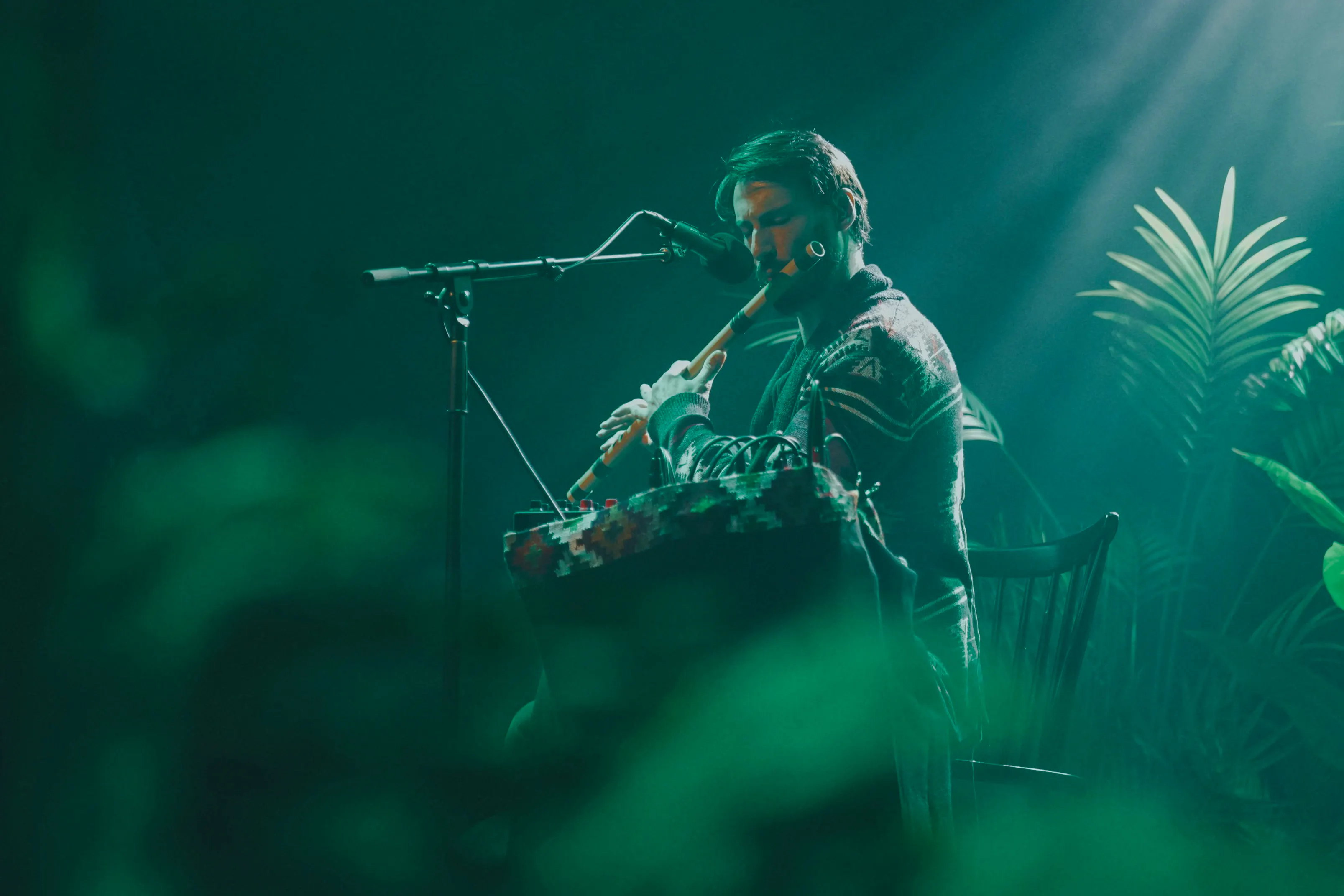 Musician playing flute on stage surrounded by plants during Medicine Music event in London.