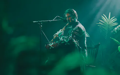 Musician playing flute on stage surrounded by plants during Medicine Music event in London.