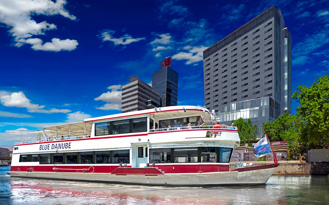 Boat on the Danube River with cityscape backdrop, part of Blue Danube Waltz tour.