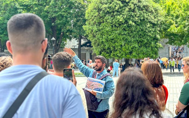 Tour guide leading a group in Istanbul's Old City, holding a map, with trees and historic buildings in the background.