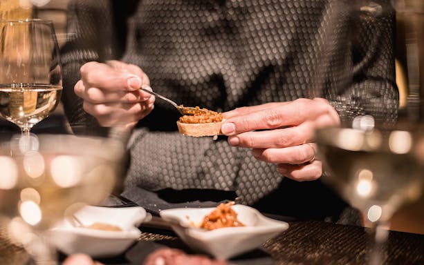 Person spreading tapenade on bread during a wine tasting in a private cellar.