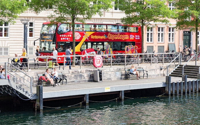Hop-On-Hop-Off bus by canal in Copenhagen with people on the promenade.