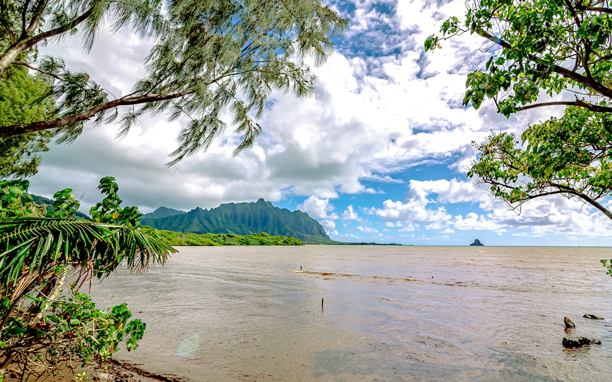 Kualoa Ranch coastline with lush greenery and distant mountains in Oahu, Hawaii.