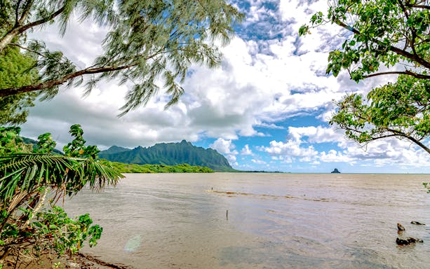 Kualoa Ranch coastline with lush greenery and distant mountains in Oahu, Hawaii.