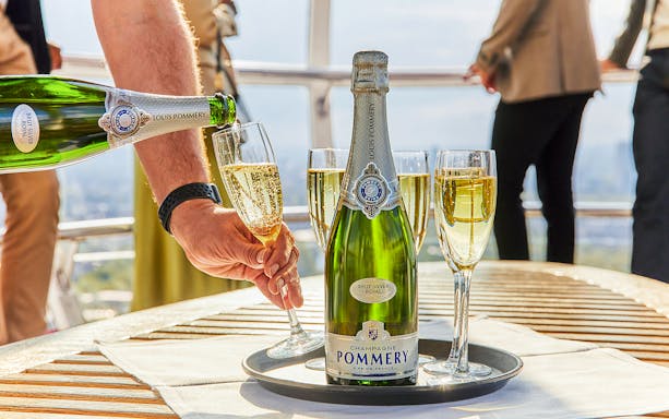 Pouring champagne on the London Eye with city view in background.