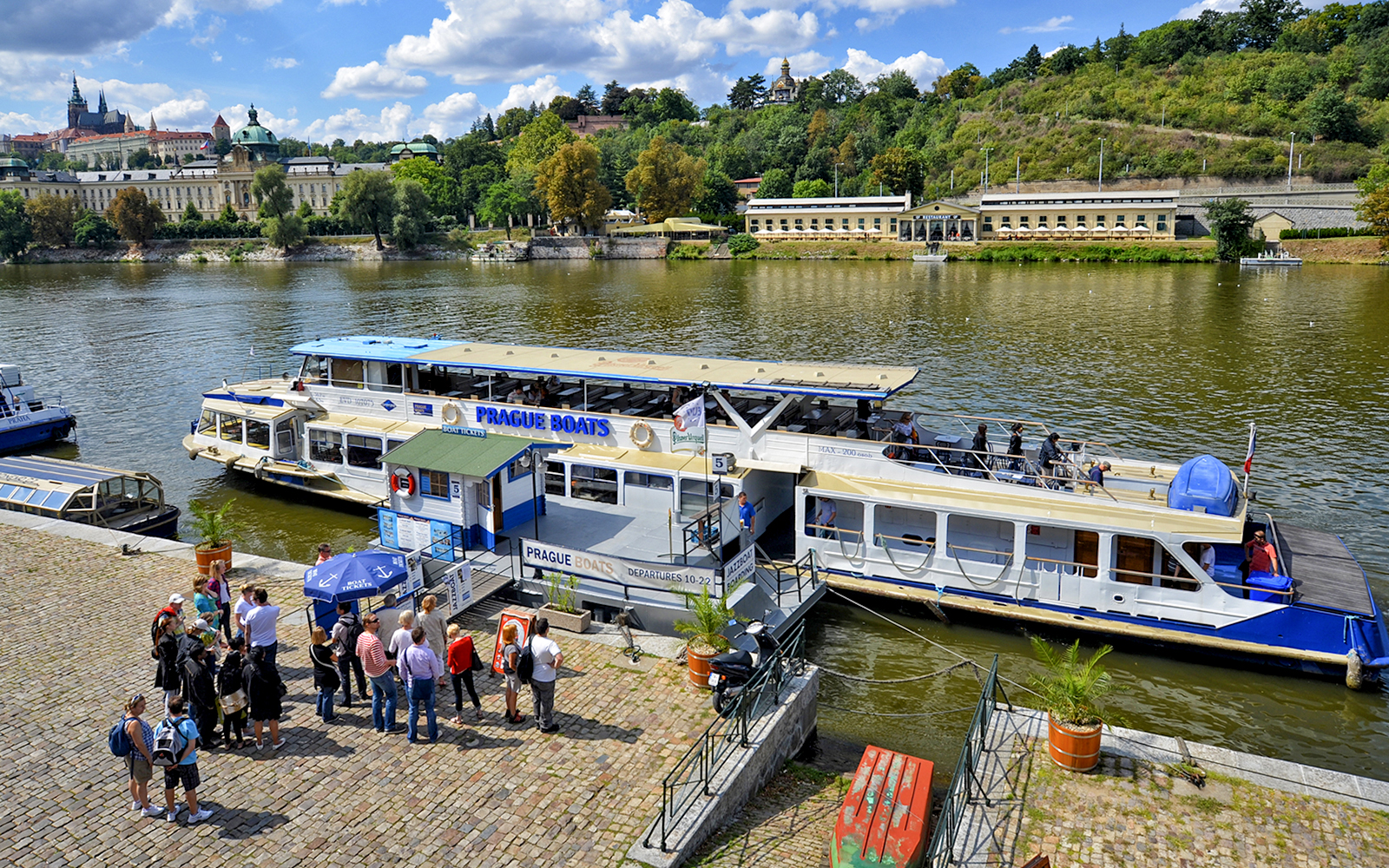 Vltava River cruise boat docked in Prague with tourists boarding.
